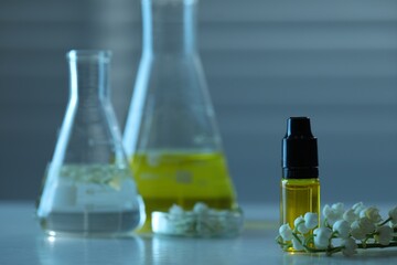 Making luxury perfume. Essential oils in glassware and flowers on white wooden table, closeup