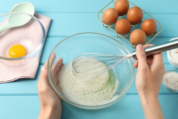 Woman whisking egg whites in bowl at light blue wooden table, above view