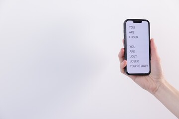 Cyber bullying. Woman holding smartphone with insults on light background, closeup. Space for text