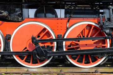Red and black wheels of an old steam locomotive standing on rails