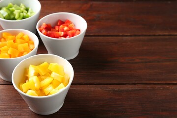 Pieces of fresh colorful bell peppers in bowls on wooden table, closeup. Space for text