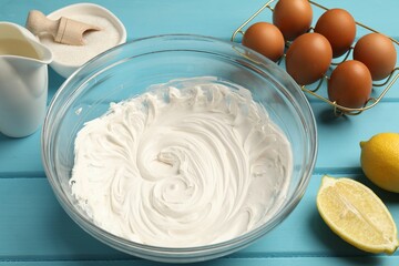 Whipped cream in bowl, eggs and other products on light blue wooden table, closeup