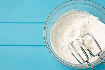 Whisks and whipped cream in bowl on light blue wooden table, top view. Space for text