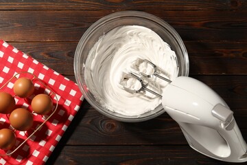 Hand mixer, whipped cream in bowl and eggs on wooden table, flat lay