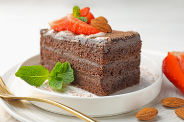 Piece of delicious chocolate cake with strawberry, almonds and mint on table, closeup