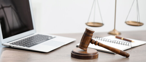 Laptop, judge's gavel and scales on wooden table in office, closeup