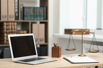 Judge's workplace with laptop, stationery and scales on wooden table in office