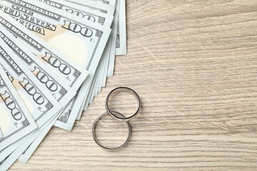 Silver wedding rings and dollar banknotes on wooden table, flat lay. Space for text