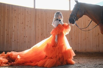 Beautiful model girl stands in a long dress with a horse