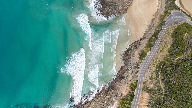 Aerial of road bending around beach with waves