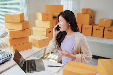 Young Asian woman experiencing stress during a phone call while working in her office, surrounded...