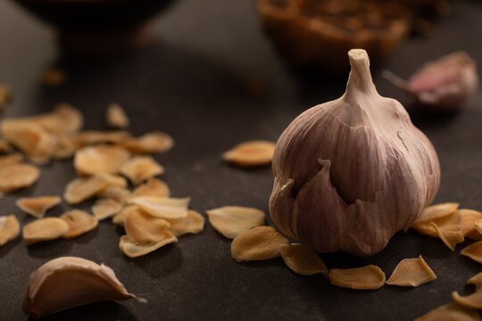 Garlic bulb and garlic chips on dark benchtop
