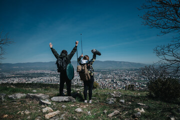 Two hikers cheerfully take in a scenic view from a hilltop, creating a serene moment against a...