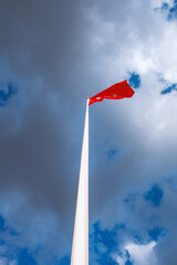 Red Flag on Tall Pole Against Blue Sky with Clouds: A Stunning Vertical Photograph