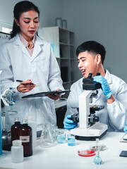 Group of young scientists in lab coats collaborate in a high-tech laboratory, analyzing samples...