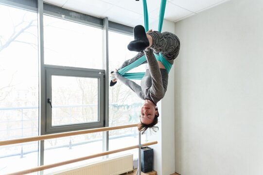 Athletic woman performing an inverted pose on teal aerial silks.