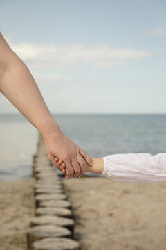 Mutter h&auml;lt die Hand ihrer Tochter am Strand &ndash; Symbol f&uuml;r Liebe und Geborgenheit