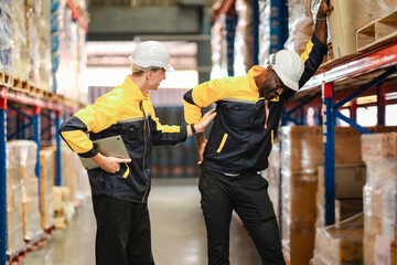 A Black man holds his lower back in pain after lifting a box, while a White coworker looks at him...