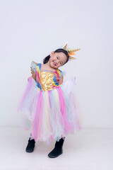 Young girl beams with joy while holding out her sparkly pastel unicorn dress doing a curtsy, full of whimsical colors and playful energy. Isolated on a light background.