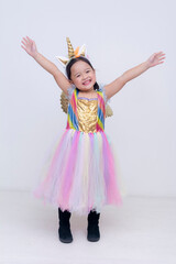 Young girl expresses pure joy with arms stretched wide in a whimsical unicorn costume, full of sparkle and pastel magic. Isolated on a light background.
