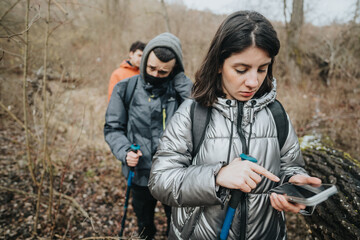 Fototapeta premium Friends explore a wooded landscape while using a smart phone to determine their path, highlighting technology's role in outdoor adventures. Teamwork and exploration are depicted in this natural