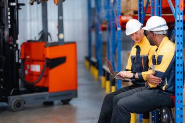 Team of male logistics workers in protective gear managing operations on laptop. Modern warehouse teamwork and digital inventory system...