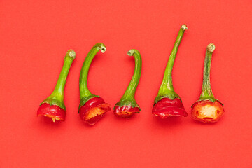 Hot red pepper tails on red background, cut parts of capsicum chilli pepper with seeds and green stalks