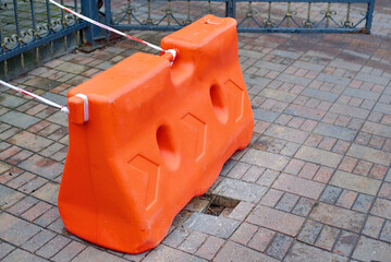 Sidewalk damage with gap in paving slabs marked by red plastic barrier block for pedestrian safety and warning of hazard in urban public walking area..