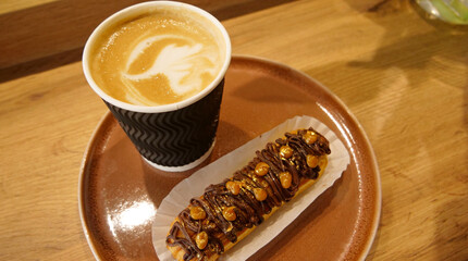 Pattern on a cappuccino foam in craft paper cup served with handmade french cake with nuts and chocolate icing at coffee shop