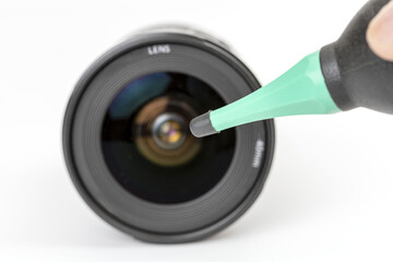Camera lens is being cleaned with dust blower, focusing on lens surface. blower has green nozzle,...