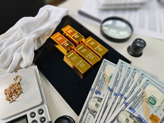 Gold bars, cash and a magnifying glass arranged on a table