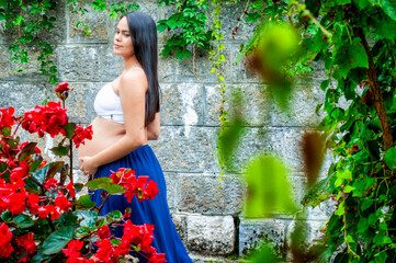 Pregnant Woman in Garden with Red Flowers and Stone Wall