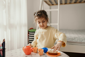 Happy Little Girl Playing with Toy Tea Set at Home. Pretend Tea Party Playtime with Colorful Toy Set in Cozy Bedroom