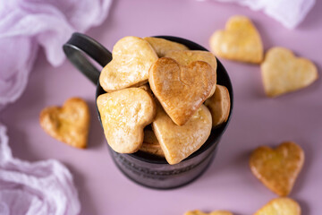 Sweet dessert: heart-shaped cookies in an iron mug. Delicious cookies for breakfast on a pink background. Close-up. View from above.