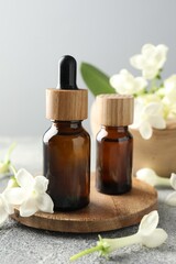 Bottles of essential oil and jasmine flowers on grey table, closeup