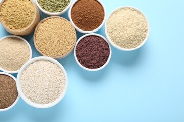 Different superfood powders in bowls on light blue background, flat lay. Space for text