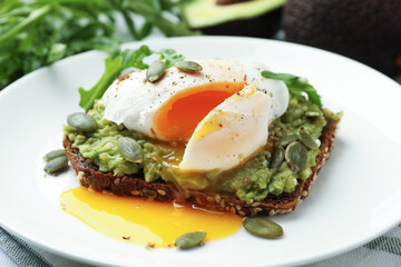 Delicious sandwich with avocado, poached egg, arugula and pumpkin on table, closeup