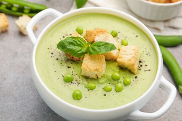 Tasty pea cream soup with croutons and basil served on grey table, closeup