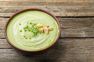 Tasty pea cream soup with croutons and thyme on wooden table, closeup. Space for text