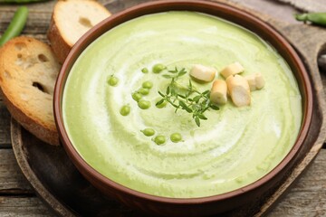 Tasty pea cream soup with croutons and thyme served on wooden table, closeup