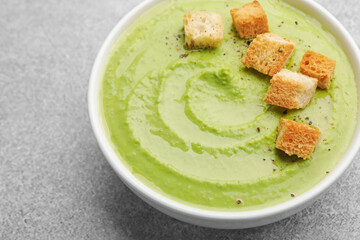 Tasty pea cream soup with croutons on grey table, closeup