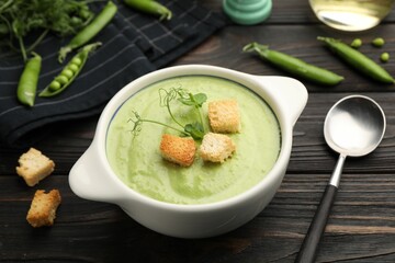 Tasty pea cream soup with croutons served on dark wooden table, closeup