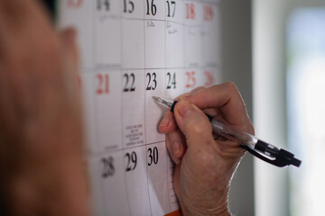 a senior woman is writing on a wall calendar in her home.