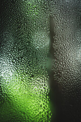 Close-up of dew droplets on a window with a blurred green forest in the background. The image captures the serene connection between humidity and nature in a peaceful, earthy atmosphere.