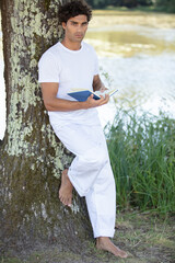 spiritual man in white clothing reads book stood by tree