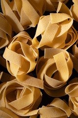 uncooked pasta nests arranged in pattern, black background, raw food