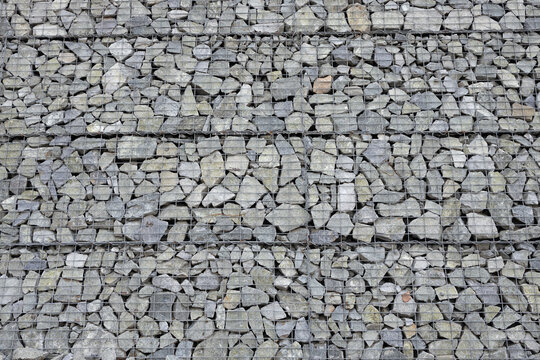 Stone wall texture made of gray rocks in a metal grid &ndash; background for architecture and construction themes