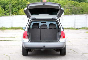 Fototapeta premium Empty Estate Car Trunk, Grey Car Trunk Ready for Loading against green trees. Modern wagon car open trunk. Car boot is open. Front view.
