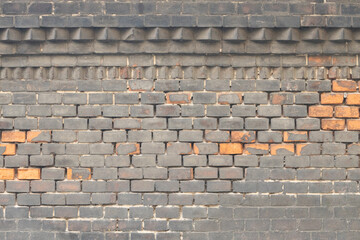 Faded dark brick wall with decorative top and scattered orange bricks