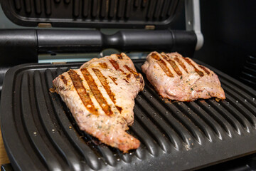 Grilled marinated meat cooking on an electric contact grill in a modern kitchen.